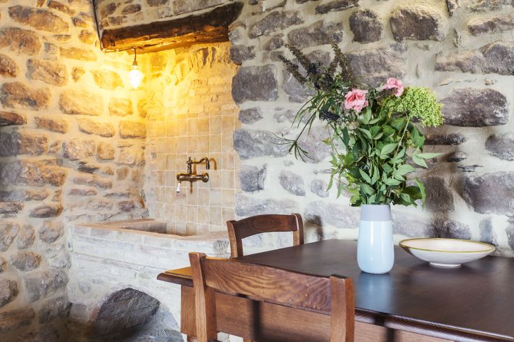 Un angolo semplice con un tavolo di legno e un vaso di fiori freschi in un ambiente rustico e luminoso.