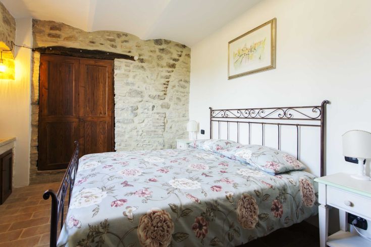 Camera confortevole con pareti in pietra e un letto matrimoniale, situata in un casolare circondato dalla natura.