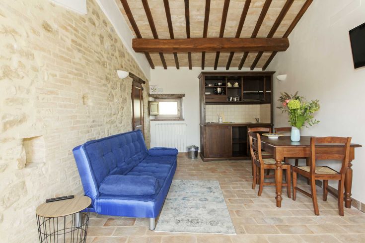 Soggiorno in stile rustico con un divano blu, un tavolo e una cucina accogliente.