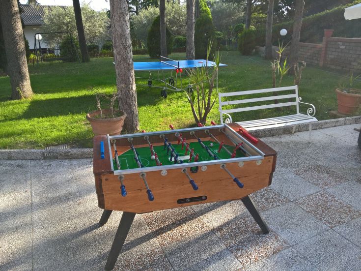 A foosball table in an outdoor area, surrounded by a peaceful and green garden.