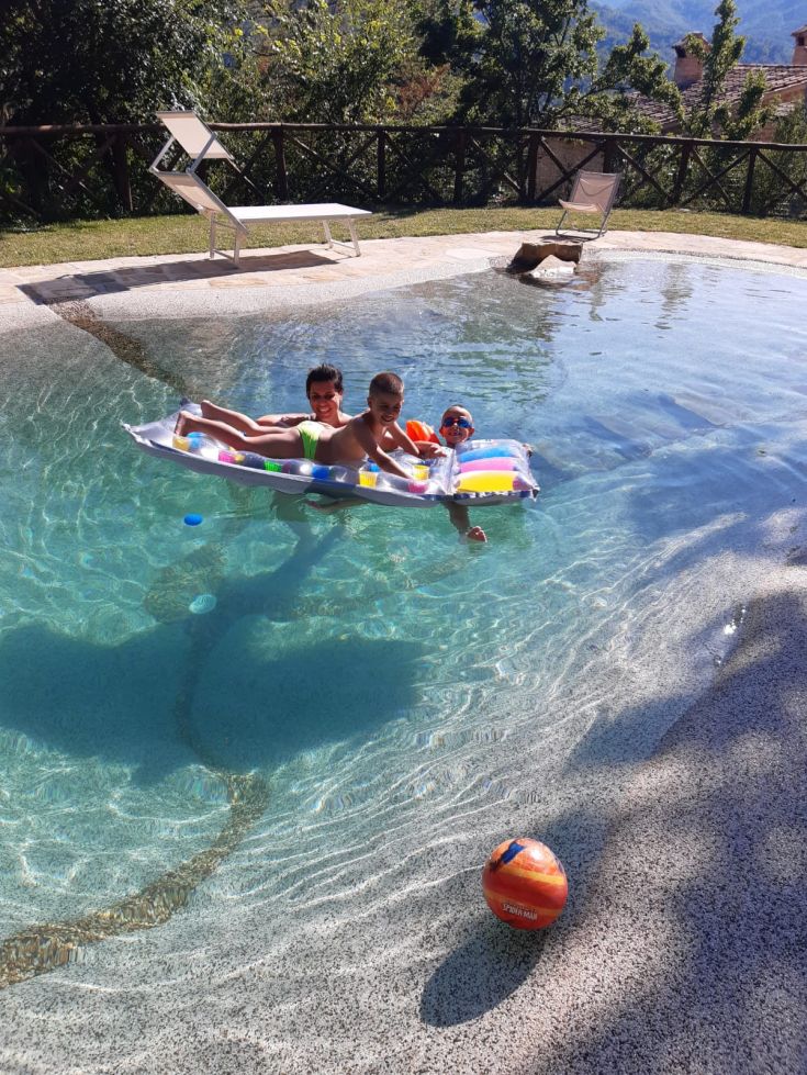 Un agréable après-midi ensoleillé au bord de la piscine avec des amis et des enfants, entourés d'arbres et de plantes.