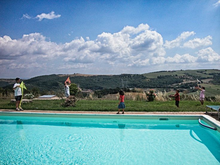 Eine Gruppe von Kindern spielt im Freien neben einem blauen Pool, umgeben von Grün.