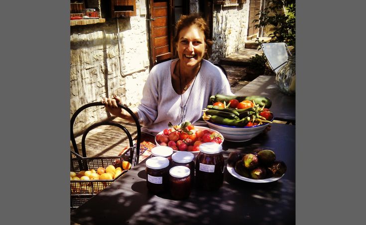 Lächelnde Frau, die frisches Gemüse und Konserven auf einem Tisch im Freien präsentiert.