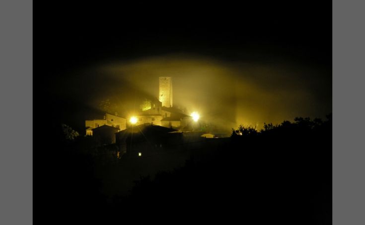 Ein ruhiges Dorf, das von Nachtlicht erleuchtet wird, mit einem historischen Turm, der aus dem Nebel herausragt.