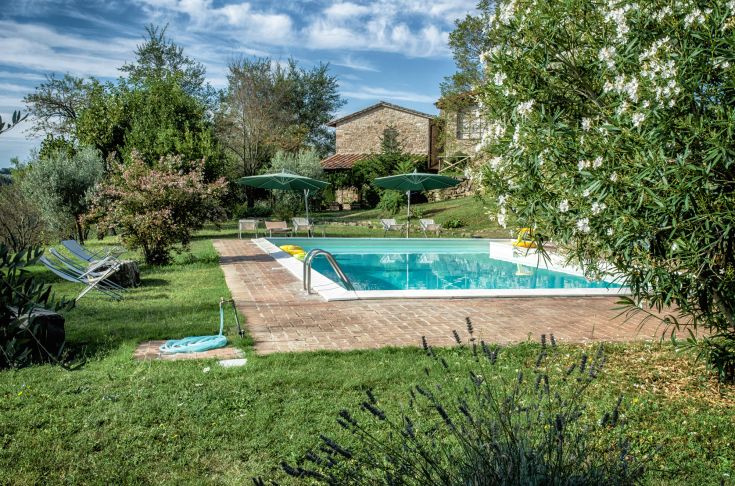 Ein steinernes Gebäude umgeben von einem Garten, mit einem Schwimmbecken im Grünen, ideal zum Entspannen.
