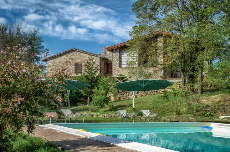 Ein Steinhof umgeben von Grünflächen, mit Pool, ideal für entspannende Momente.