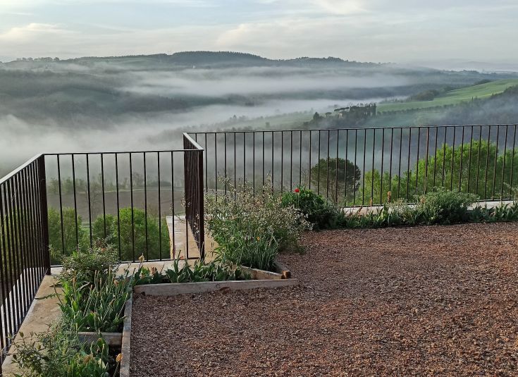 Eine malerische Aussicht auf nebelverhangene Hügel mit Blumen und einem Geländer im Vordergrund.