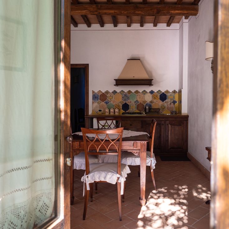 Cucina semplice con elementi in legno e piastrelle decorate, immersa nel verde della campagna.