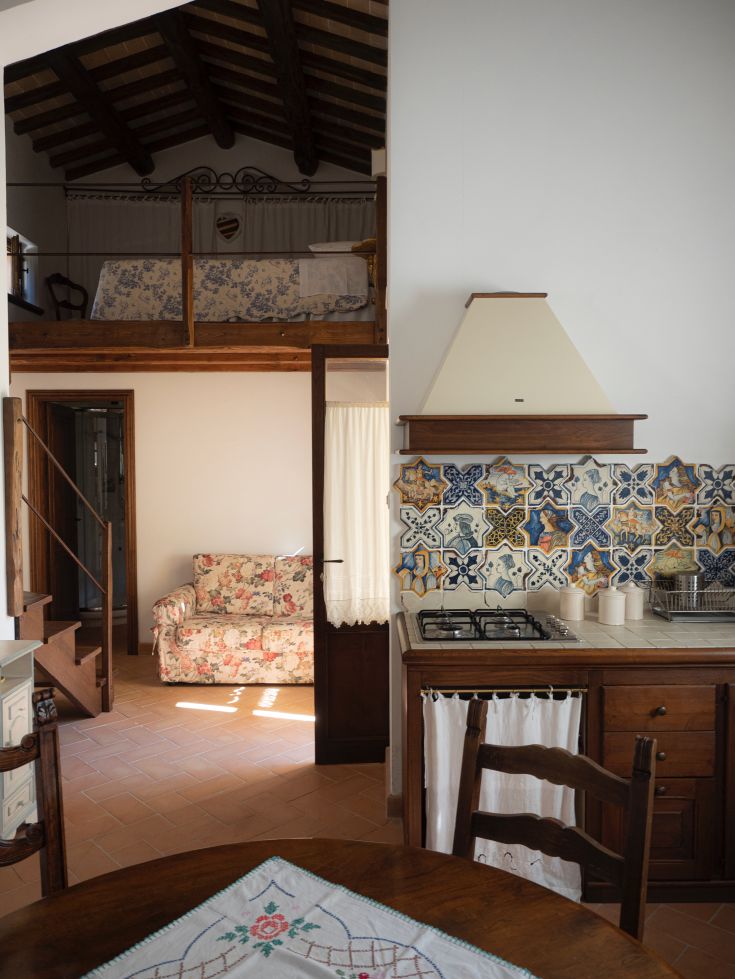 Interno di un agriturismo con area cucina, zona giorno e soppalco, arredato in legno e con piastrelle tradizionali.