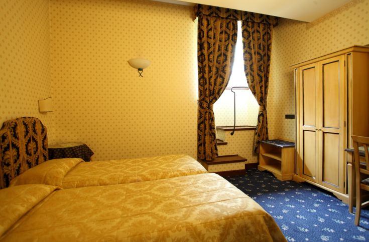 Simple hotel room with tasteful beds, light curtains, and light wood furniture.