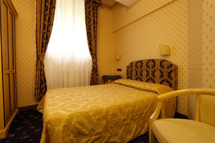 A simple hotel room with light curtains and wooden furniture.
