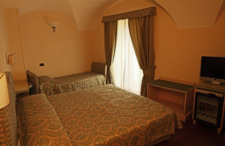 Spacious room with two beds, featuring a TV and windows for natural light.