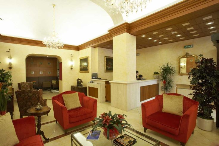 Hall dell'Hotel dei Priori, arredata con divani rossi e elementi decorativi classici.