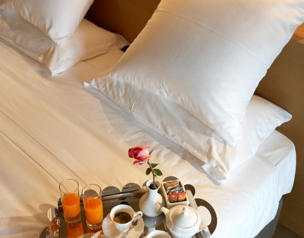 Colazione servita su un vassoio in un letto comodo, con bevande fresche e fiori decorativi.