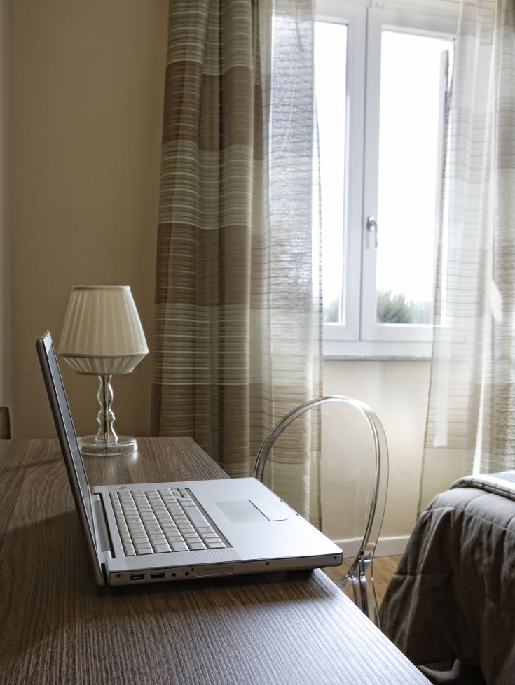 Un angolo di lavoro semplice con un laptop e una lampada, illuminato dalla luce naturale che entra dalla finestra.