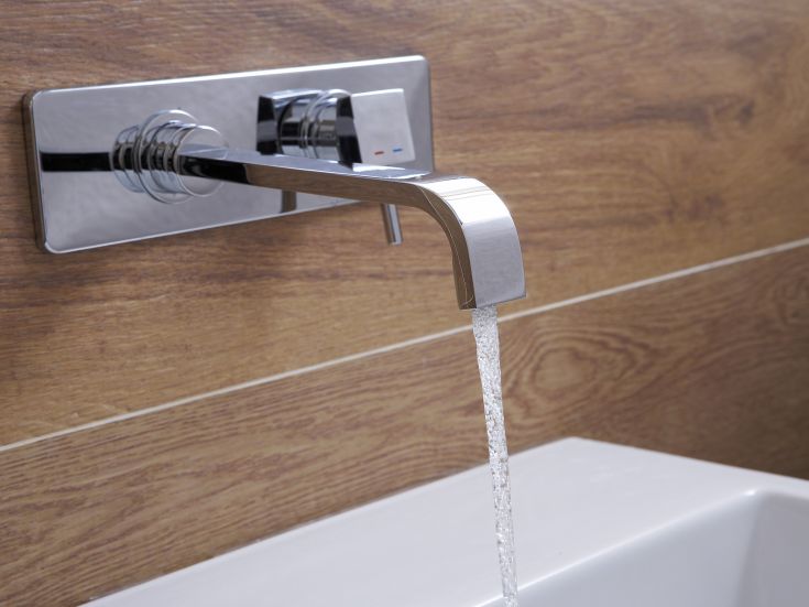 Rubinetto in acciaio cromato con acqua che scorre, posizionato su un ripiano in legno.