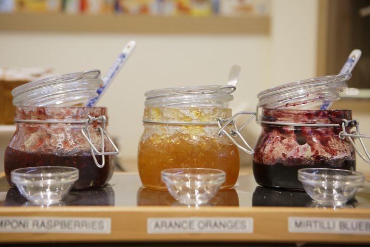 Vasetti di confettura di frutta mista disposti su un tavolo, pronti per essere serviti a colazione.