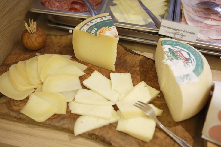 Fette di formaggio disposte su un tagliere di legno, con una forma intera al lato.