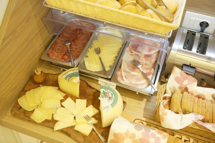 Colazione con formaggi, salumi e pane fresco in un'atmosfera calda e confortevole.