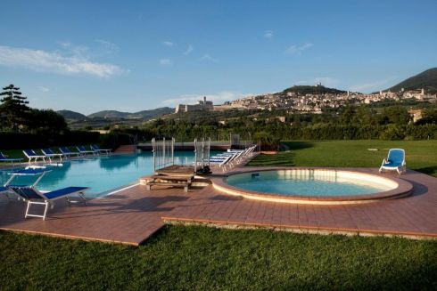 Riposo e benessere in un hotel vicino a Assisi, con panorama sulle colline e piscina circondata da vegetazione.
