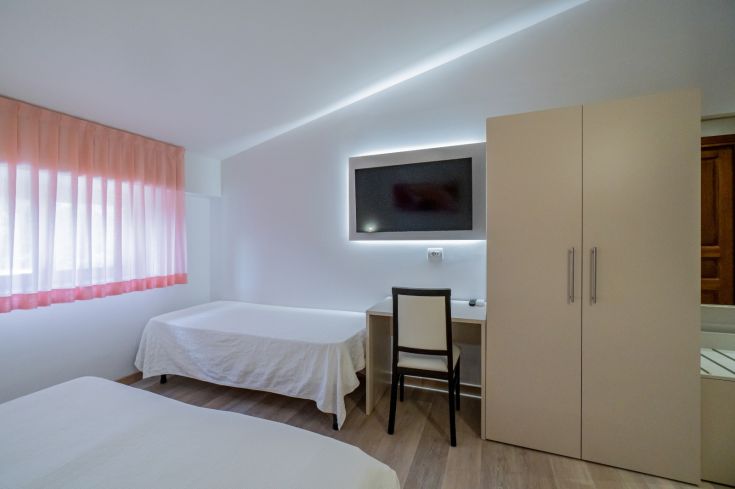 Camera moderna e ben illuminata con due letti singoli, arredamento sobrio e televisore disponibile.