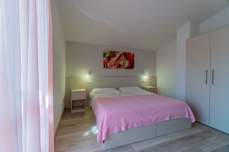 Camera semplice con letto matrimoniale, ben illuminata e arredamento funzionale.