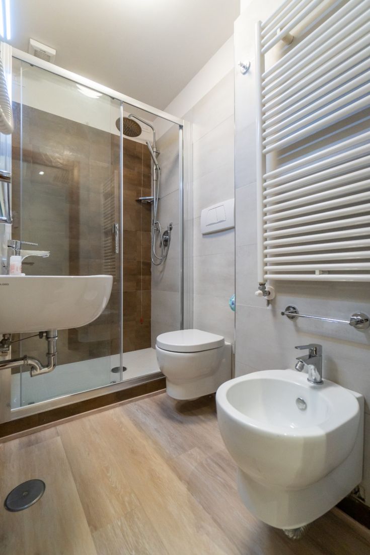 Bagno dal design contemporaneo, dotato di doccia, sanitari funzionali e pavimento in legno chiaro.