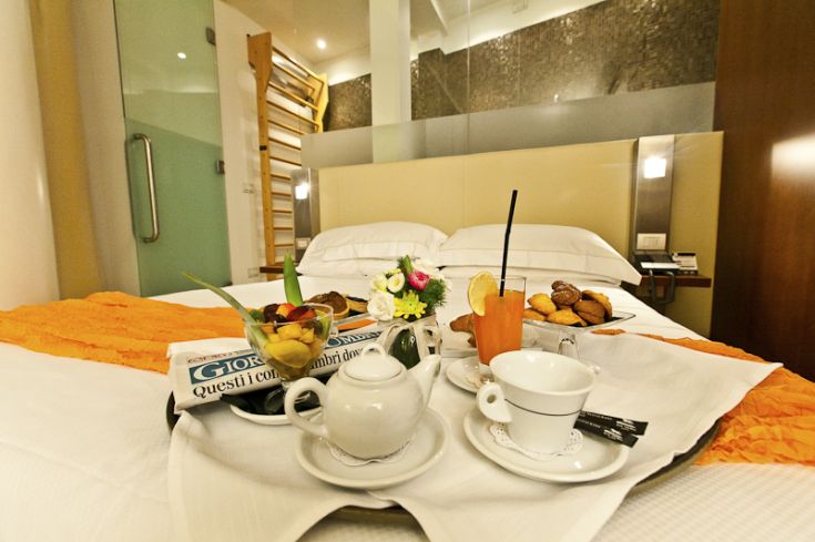 A simple designed hotel room with a tray featuring breakfast and fresh fruit.