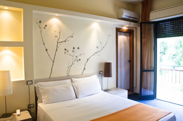 Camera sobria con decorazioni semplici, luce naturale e accesso a un piccolo balcone.