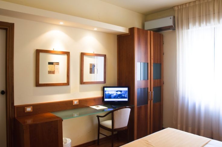 Camera spaziosa e ben illuminata, dotata di scrivania, televisore e elementi decorativi contemporanei.