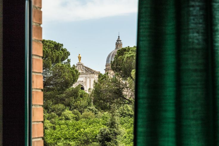 Panorama della chiesa visto attraverso una finestra verde, contornata da alberi e vegetazione.