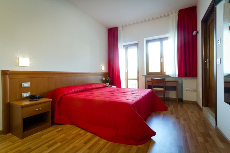 Camera semplice con letto rosso e mobilio contemporaneo, ambiente luminoso e rilassante.