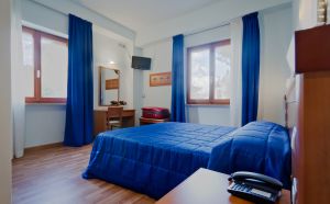 Camera di un hotel con letti blu, finestre ampie e arredamento sobrio.