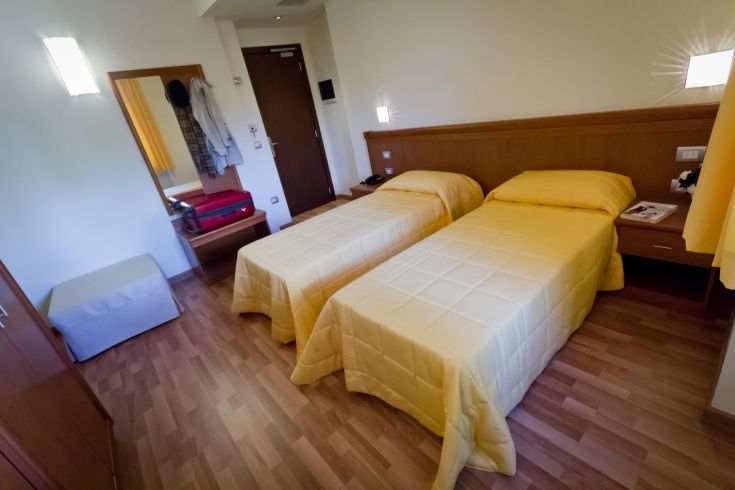 Camera confortevole con letti singoli e arredi pratici, illuminata da luci tenui.