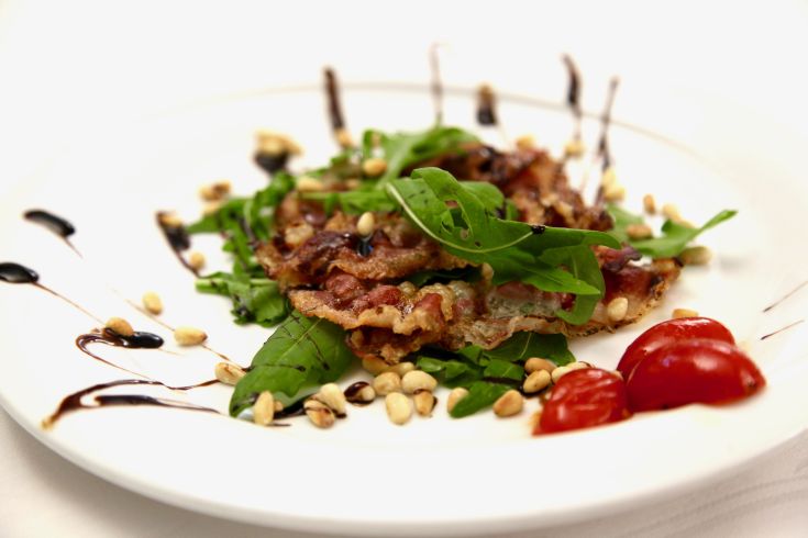 Un piatto con fette di bresaola, rucola fresca, pinoli tostati e pomodorini, adatto per un pranzo leggero.