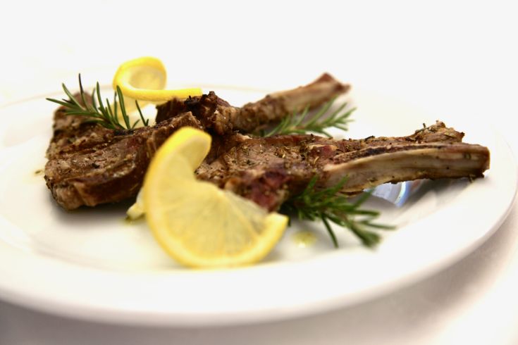 Costolette di agnello accompagnate da fette di limone e rametti di rosmarino, pronte per essere servite.