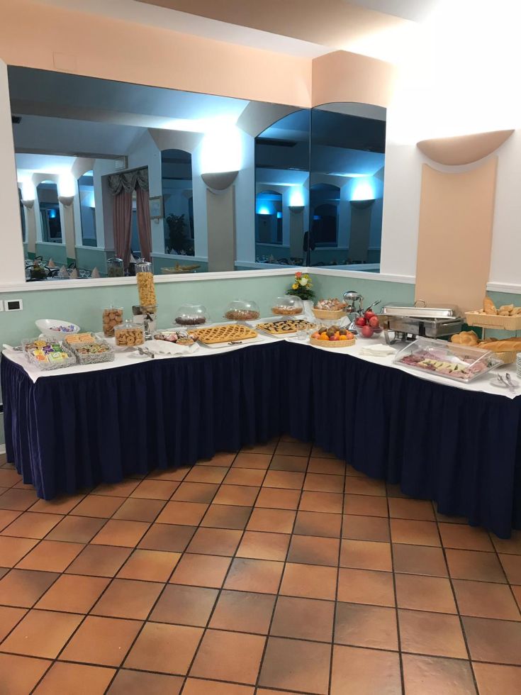 Buffet assortito di dolci e frutta, disposto in un ambiente luminoso e confortevole.