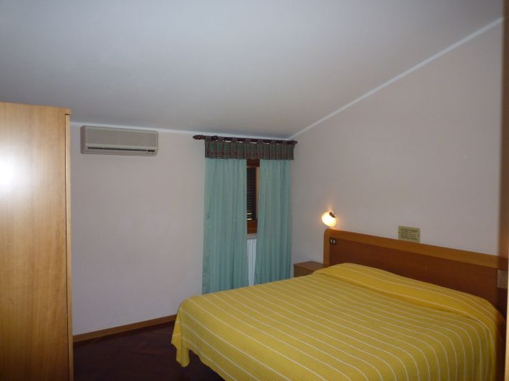 Camera accogliente con letto matrimoniale, ornata con tende chiare e arredi semplici.