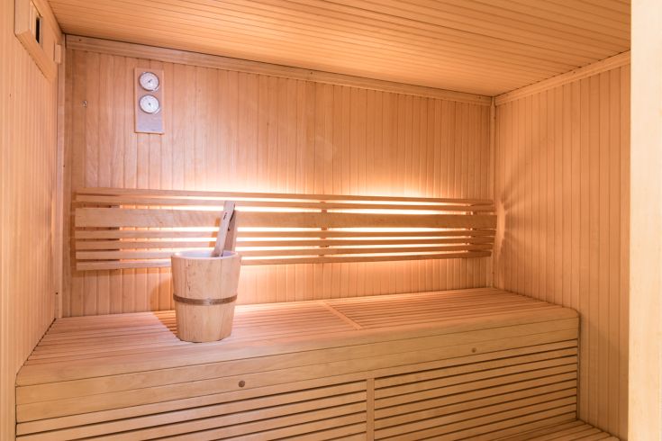 Interior of a simple wooden sauna with a bench and bucket, illuminated by soft lighting.