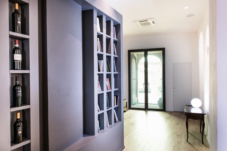 A simple interior featuring a wooden shelf, wine bottles, and natural light illuminating the space.
