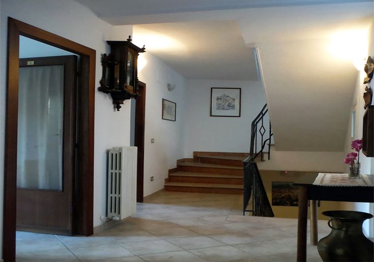 Interno di un palazzo, con arredi in legno e scale in pietra. L'ambiente è luminoso e accogliente.