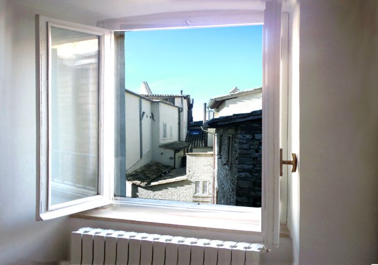 Scena dei tetti di Assisi e del cielo vista da una finestra di un palazzo storico.