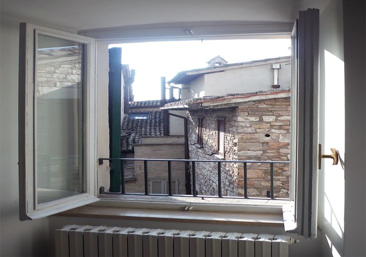 Scena che mostra antiche case di Assisi attraverso una finestra aperta, rappresentando l'atmosfera del centro storico.