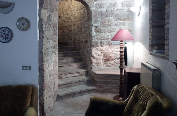 Ambiente interno di un palazzo medievale, dotato di scale in pietra e arredi sobrii e funzionali.
