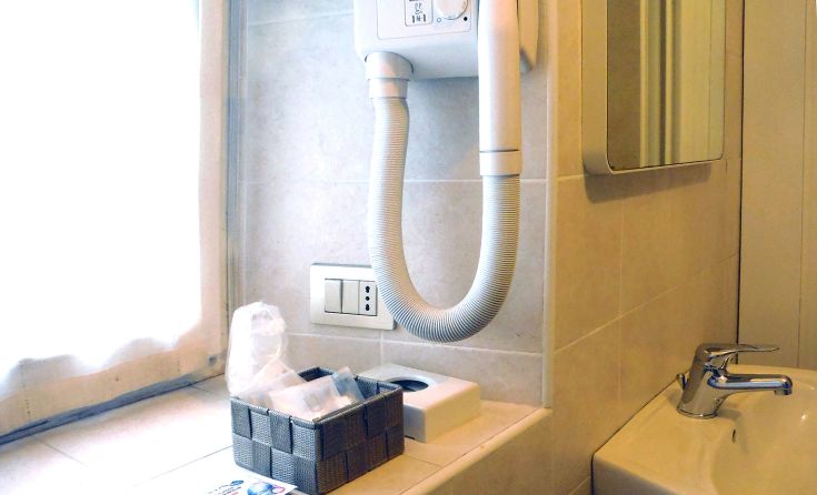 Bagno moderno con asciugacapelli a muro e articoli da toeletta disposti in modo funzionale. Ambiente pratico e ben arredato.