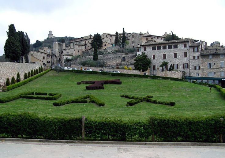 Scena di Assisi, con giardini ben curati e case in stile medievale che caratterizzano l'architettura della zona.