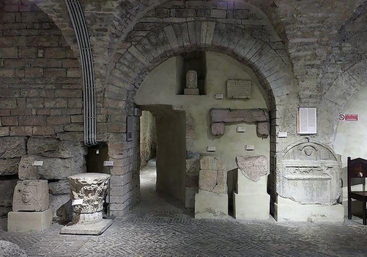 Collezione di reperti storici allestita in un ambiente di epoca medievale, caratterizzato da strutture in pietra.