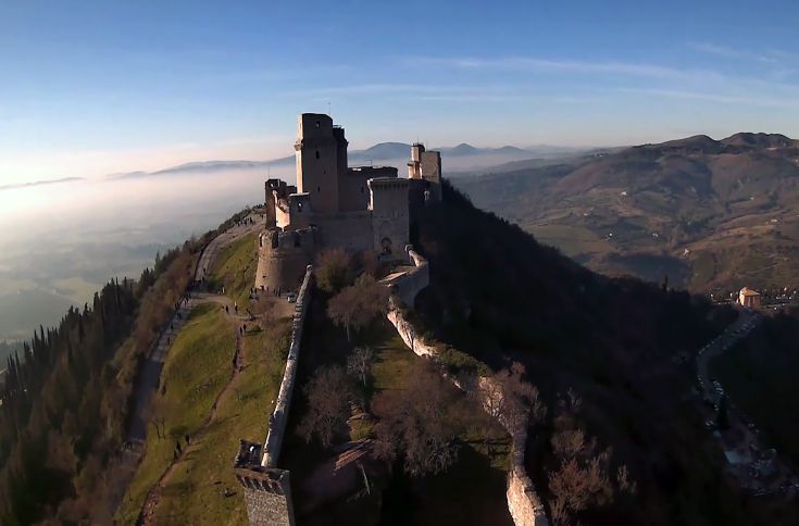 Castello medievale situato su una collina, circondato da un paesaggio naturale.