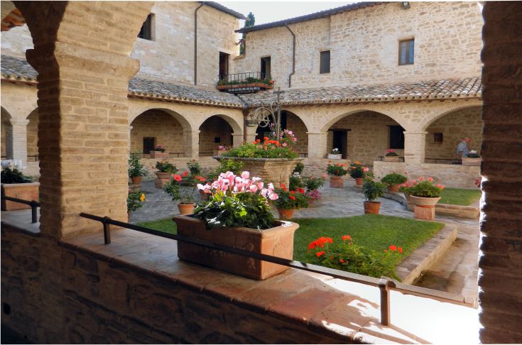 Un chiostro con fiori che circondano una struttura in pietra, semplice e accogliente.