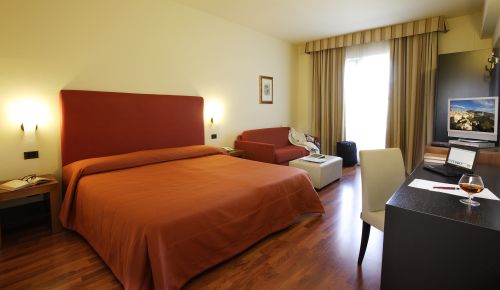 Spacious and modern hotel room with wooden flooring and views of Umbrian landscape.